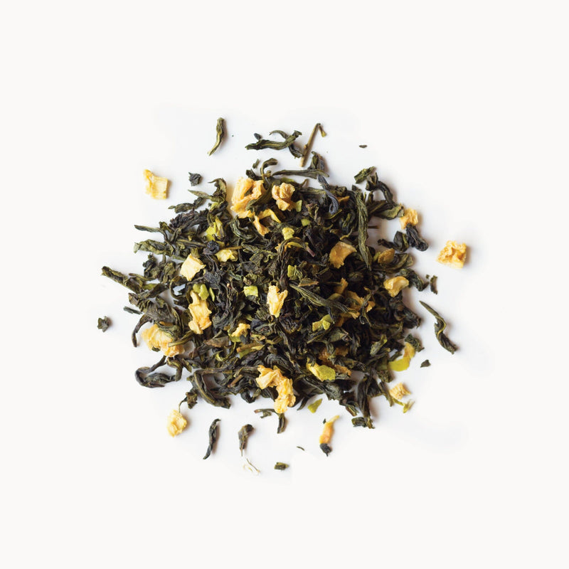 A pile of loose leaf Tropical Coconut Oolong tea from Rishi Tea & Botanicals, adorned with lush green leaves and dried yellow flower pieces, lays beautifully on a white background.