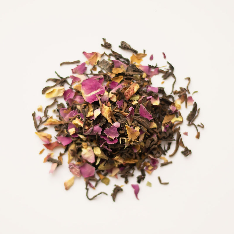 A pile of Rose Hawthorn Pu’er petals on a white background, accompanied by a cup of traditional Shu Pu'er tea from Rishi Tea & Botanicals.