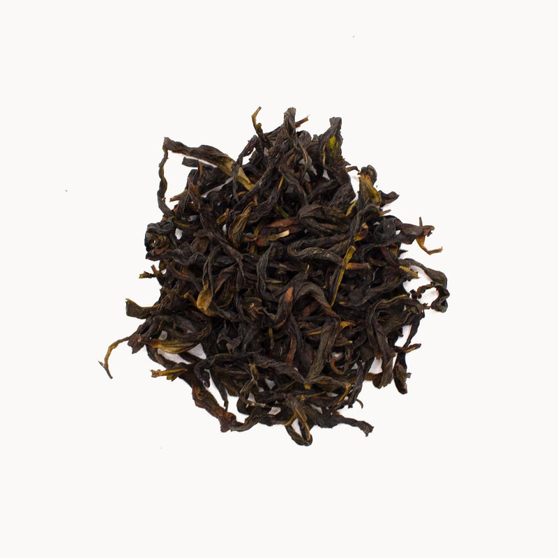 A small pile of limited-edition Phoenix Dancong Yin Hua Xiang tea leaves scattered against a plain white background, beckoning connoisseurs with their rich, dark essence from Rishi Tea & Botanicals.